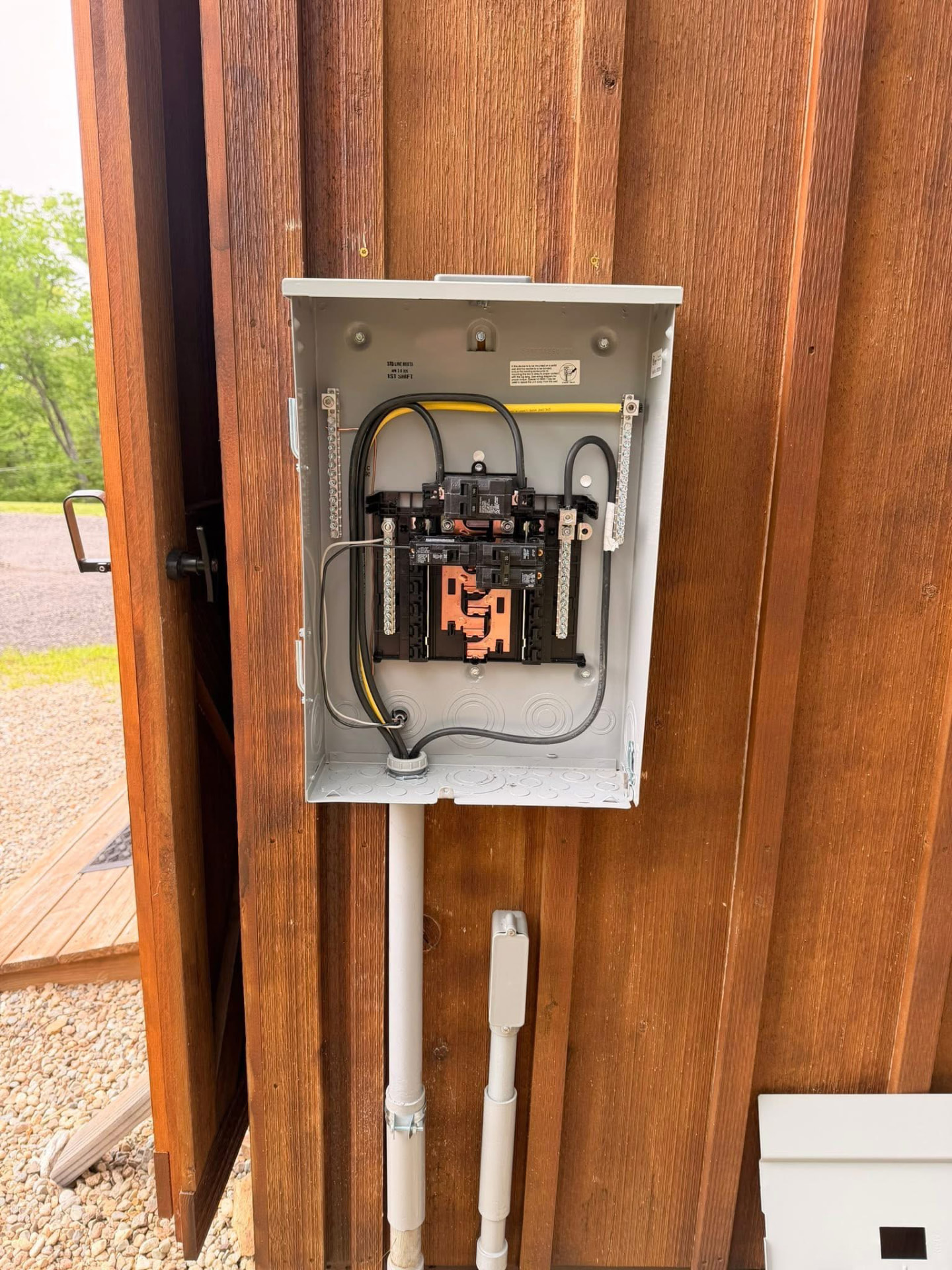 Outdoor subpanel installed on cedar siding with conduit runs